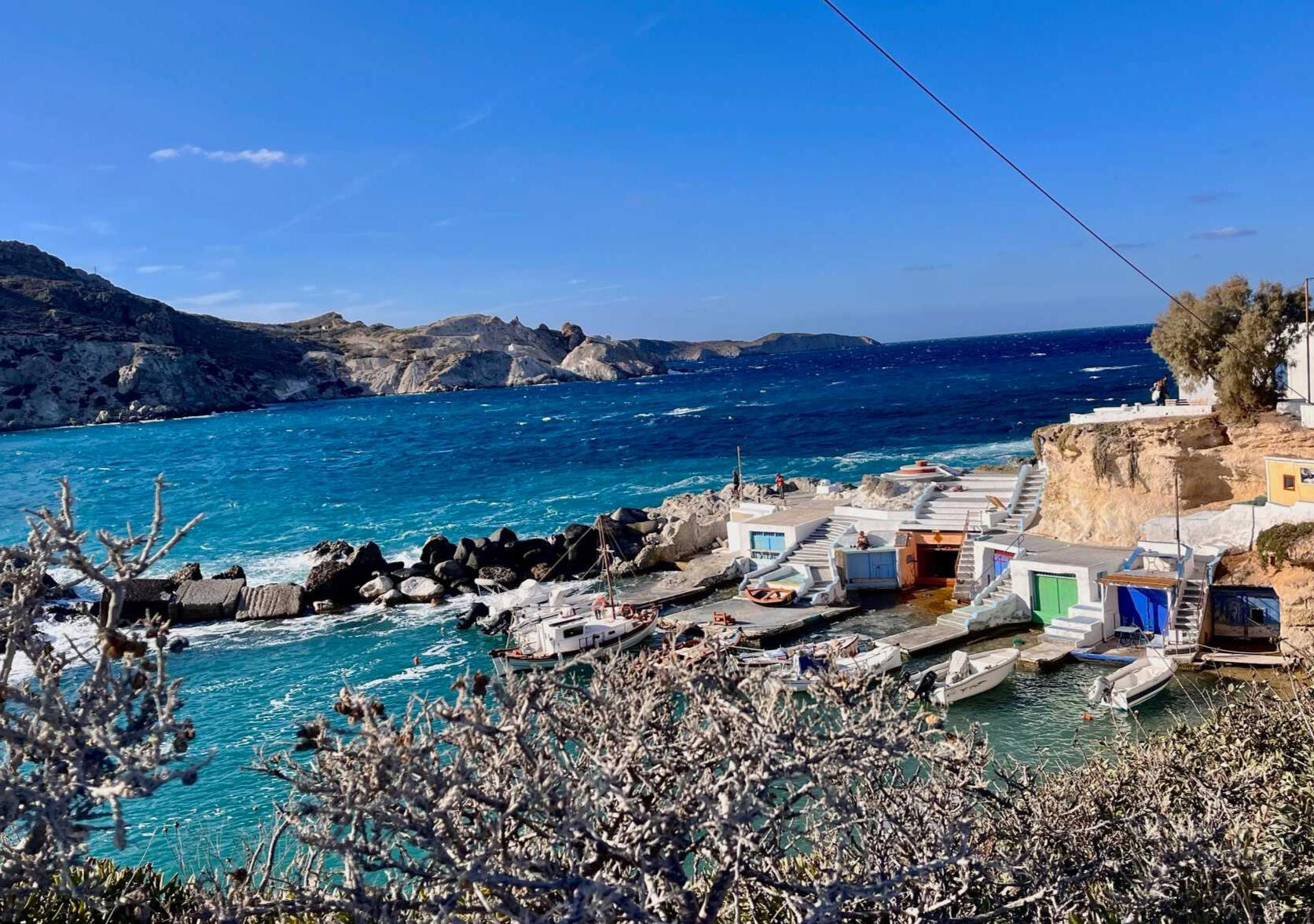 Mandrakia in Milos Greece, photo taken by Mia's Photography and Events. Colourful blue and green doors on the boat houses, little boats and crystal blue water.